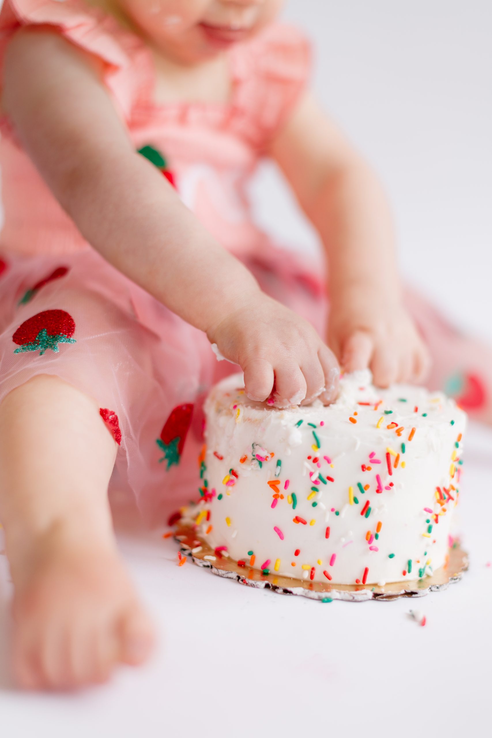 baby girl hands reaching for birthday cake during cake smash session - St Louis milestone photographer